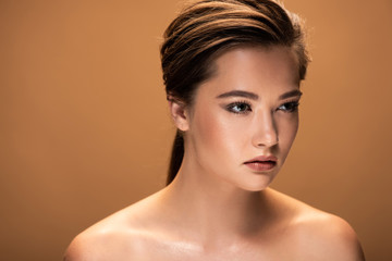 young beautiful naked woman with shiny makeup looking away isolated on beige