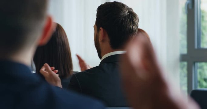 Back view on the Caucasian people in business style applauding to the speaker at the conference. Close up.