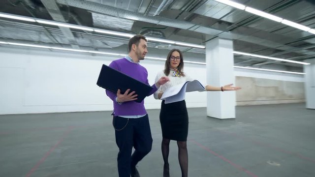 Two partners are discussing construction project of an empty hall