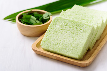 Sliced pandan bread on wooden plate and sliced pandan leaf in a bowl on white background