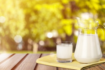 Glass and jug of milk with green meadow on background
