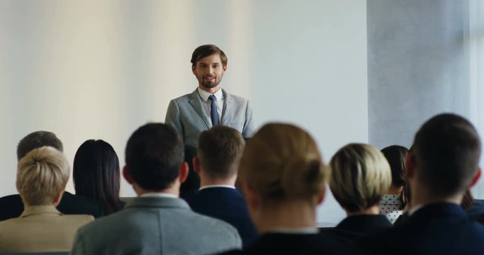 Professional male Caucasian business trainer standing in front of the audience and explaining some information to the people at the big meeting.