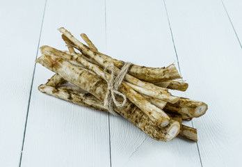 Medicinal raw burdock root on a white wooden table.
