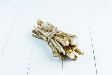 Medicinal raw burdock root on a white wooden table.