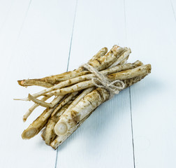 Medicinal raw burdock root on a white wooden table.