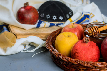 rosh hashanah jewesh holiday concept - shofar, torah book, honey, apple and pomegranate over wooden table. a kippah a yamolka