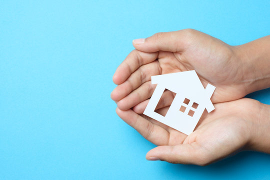 Paper house in hand palm on blue background for real estate property industry