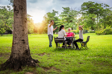 Happy asian family in outdoor park,father,mother with cute child girl or daughter play,dancing,elderly woman having fun,laugh,smile together,senior grandmother in wheelchair with her family in nature