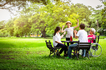 Happy asian family in outdoor park,father,mother with little child girl or daughter play,dancing,singing,elderly woman having fun,laugh,smile together,senior grandmother in wheelchair with her family 