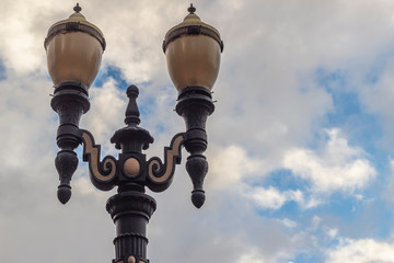 Fototapeta na wymiar Street lamps against a cloud filled blue sky