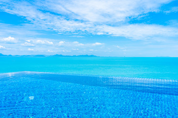 Beautiful luxury outdoor infinity swimming pool with tropical sea ocean and white cloud blue sky background