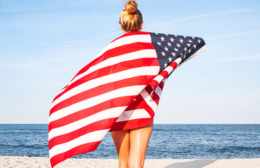 Beautiful patriotic woman with American flag on the beach.  USA Independence day, 4th July. Freedom concept.