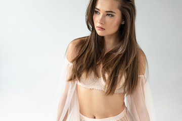 Obraz premium delicate young woman in beige lingerie with mesh sleeves looking away isolated on white
