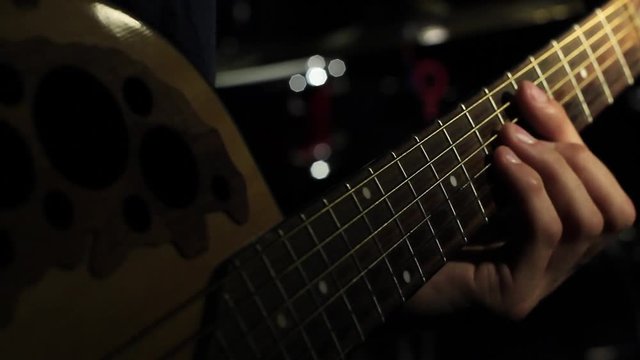 Close up of guitarist hand on acoustic guitar strings playing chords under spotlight