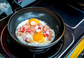 Fried eggs and ham in the pan on the gas oven.