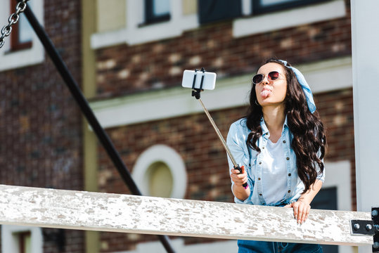 Young Woman Holding Selfie Stick And Taking Selfie While Showing Tongue