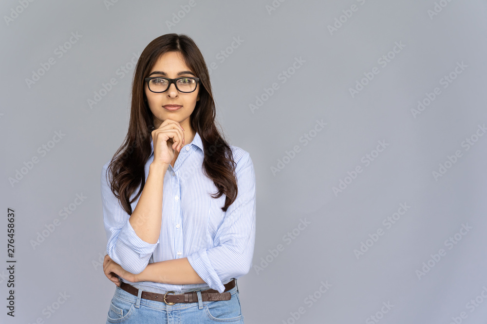 Wall mural serious thoughtful doubtful indian young business woman wear glasses hold hand on chin look at camer