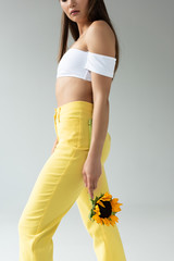 side view of woman in yellow pants posing with sunflower isolated on grey