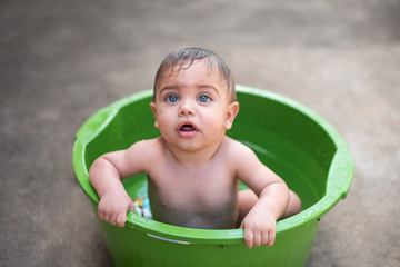 Blue-eyed baby bathing in green bucket