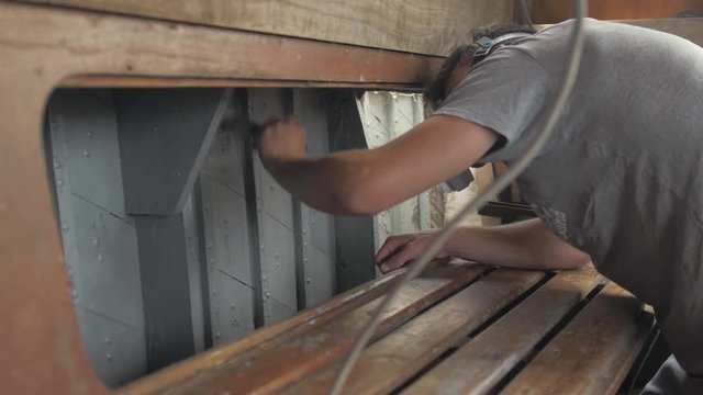 Young man painting interior of wooden boat with aluminium wood primer