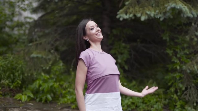 Young attractive woman is slowly dancing in solo in front of a green trees. Woman has very smooth movements. She is posing for the photos.
