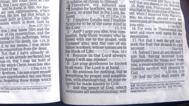 Close up of a man holding and reading the bible on his lap in philippians chapter four.