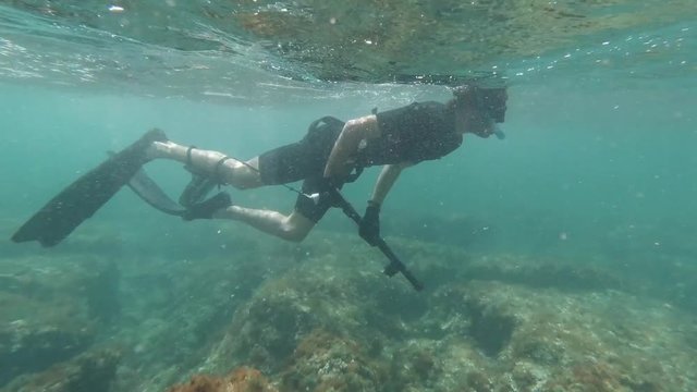 Front facing shot of spearfisher snorkeling in shallow crystal clear waters in the mediterranean sea while waves crush at shore