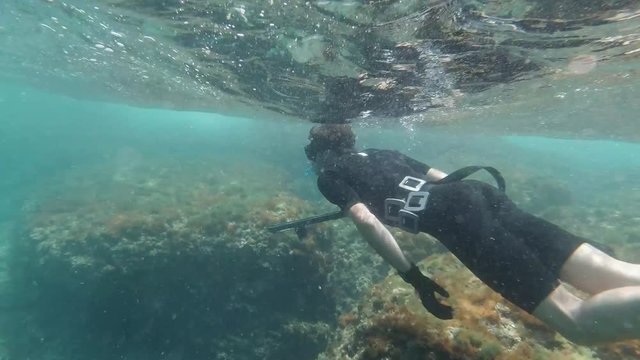 Spearfisher snorkelling in shallow water looking for fish in slow motion