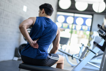 Young man having back pain after workout at the gym.