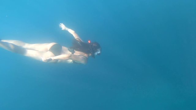 Slim, caucasian woman swimming in slow motion underwater in the deep, blue ocean of malta with fins and snorkel. The gentle light beams are reflecting through the water.