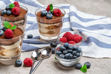 Classic tiramisu dessert with blueberries and raspberries in a glass cup on concrete background