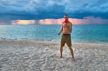Man juggles a ball on a sandy beach on the background of stormy clouds and sunset over sea                   