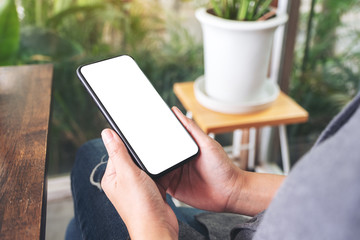Mockup image of a woman holding and using black mobile phone with blank desktop screen in cafe