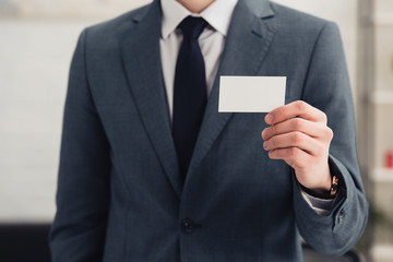 cropped view of businessman in formal wear holding blank business card