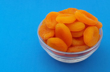 Dried apricots fruits in glass bowl on blue background with space for text
