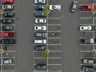 Aerial top view of parking lot at supermarket with with varieties of colored vehicles. People walking to their car and trying to park. © Unwind