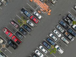 Aerial top view of parking lot at supermarket with with varieties of colored vehicles. People walking to their car and trying to park.