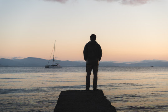 A man standing on a dock during sunrise on Kos, Greece with a boat in the background. 
