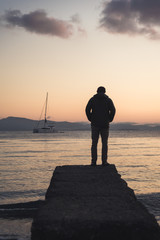 A man standing on a dock during sunrise on Kos, Greece with a boat in the background. 