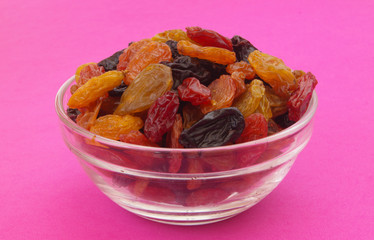 Mixed raisins in glass bowl close up on pink background