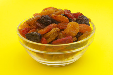 Raisins in glass bowl on yellow background