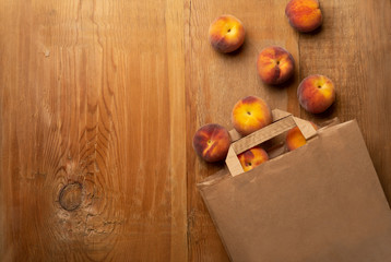 Fresh ripe peaches fruits in paper bag on wooden rustic background. Top view.