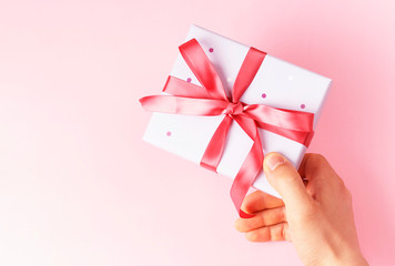 Male hand holding gift box with ribbon on pink background, top view