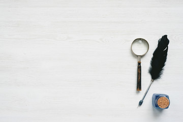Magnifying glass, quill pen and ink well on a white wooden table background with copy space....
