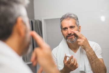 smiling middle aged bearded man applying face cream