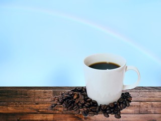 Coffee cup  and bean  on wooden floor with rainbow sky