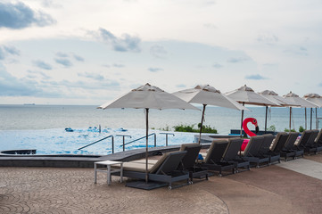 Fototapeta na wymiar Sunbed with parasol on infinity pool in tropical sea