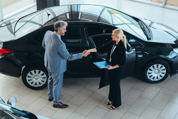 top view of sales agent shaking hand with customer in car dealership showroom