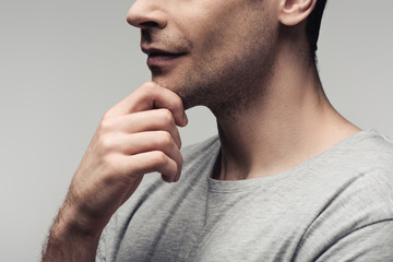 partial view of serious man holding hand near face isolated on grey, human emotion and expression concept