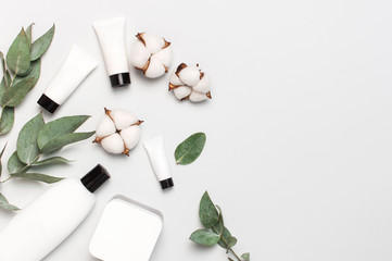 Cosmetics SPA branding mock-up. White cosmetic bottle containers with cotton flowers, eucalyptus twigs on gray background top view flat lay. Natural organic beauty product concept, Minimalism style